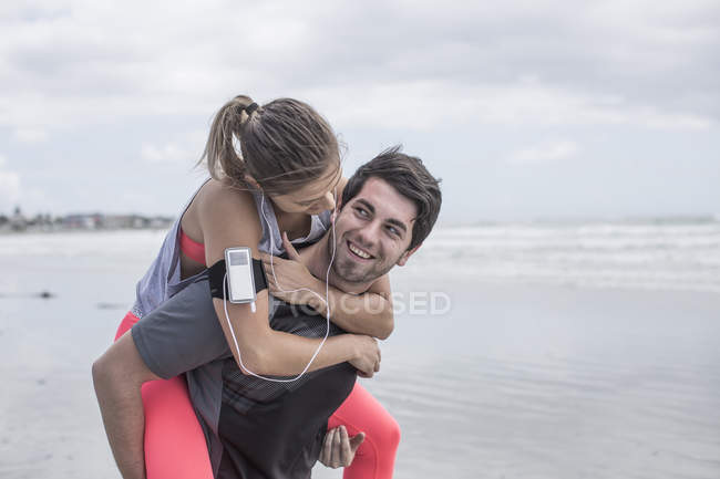 Jovem carregando namorada piggyback na praia — Fotografia de Stock