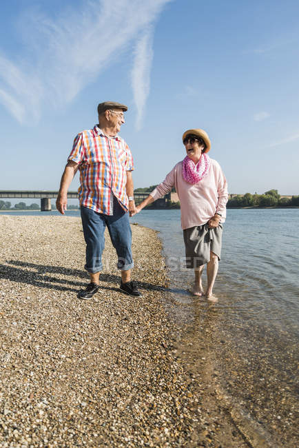 Felice coppia anziana camminando mano nella mano a riva del fiume — Foto stock