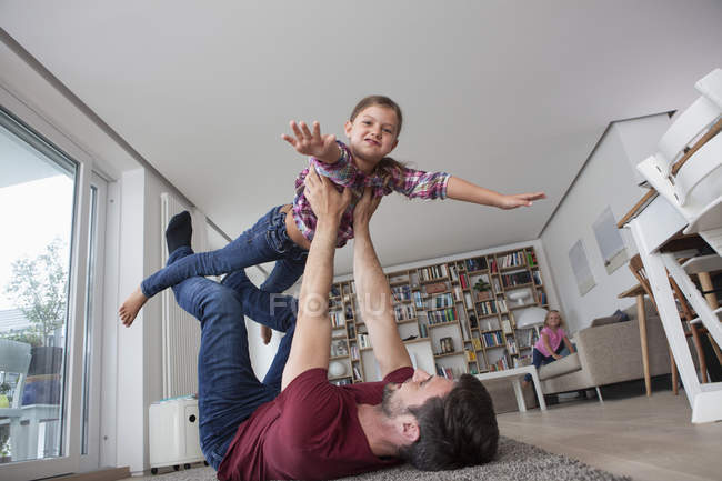 Uomo sdraiato sul pavimento in salotto a giocare con la sua piccola figlia — Foto stock