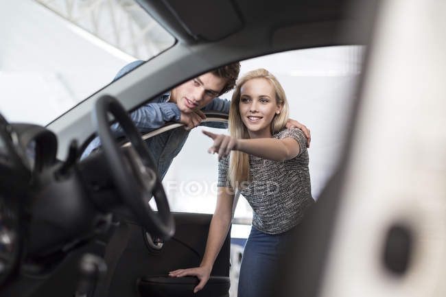 Pareja joven examinando coche nuevo en concesionario de automóviles - foto de stock