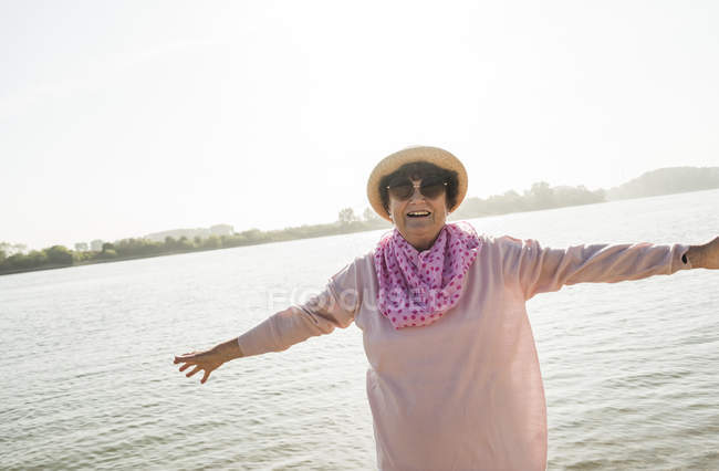 Portrait d'une femme âgée souriante aux bras tendus devant une rivière — Photo de stock