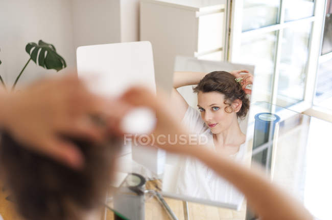 Femme regardant dans le miroir mettant des fleurs dans ses cheveux — Photo de stock