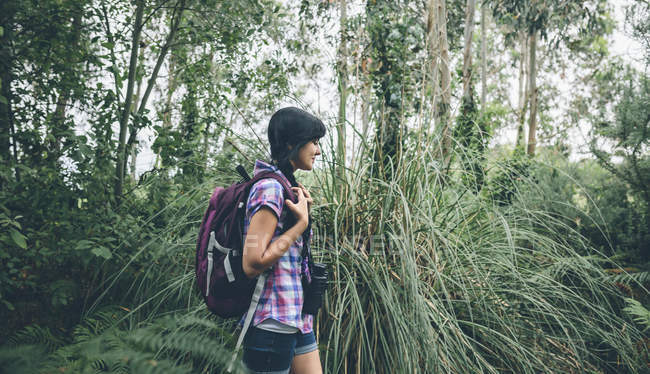 Lächelnde junge Frau mit Rucksack spaziert im Wald — Stockfoto