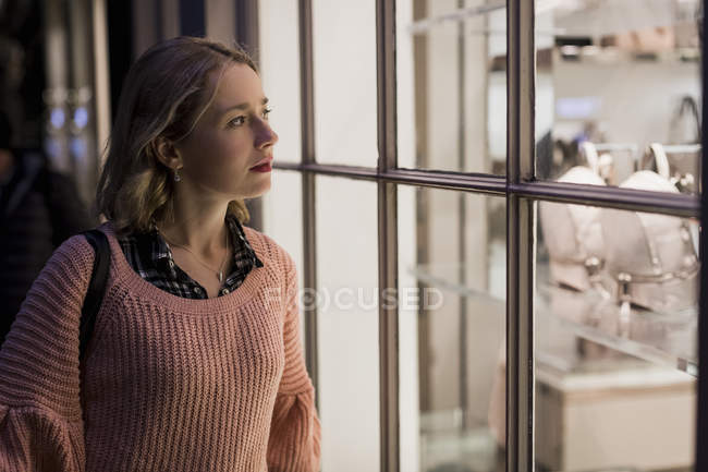 Portrait de jeune femme regardant dans la vitrine dans la soirée — Photo de stock
