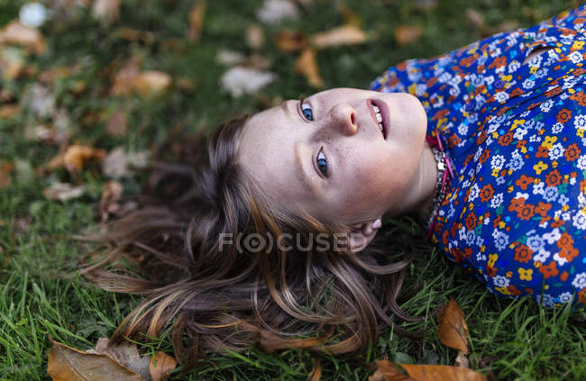 Retrato de menina deitada em um prado e olhando para a câmera — Fotografia de Stock