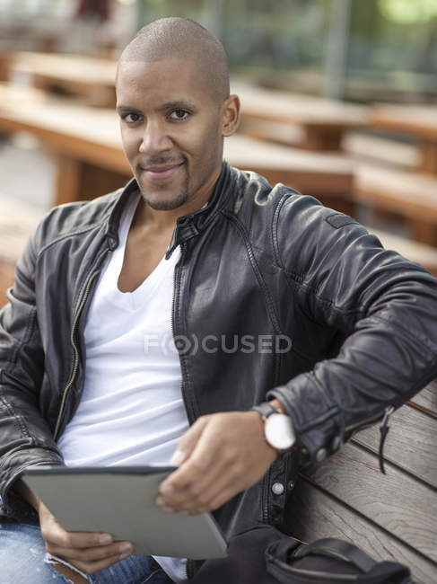 Joven sentado en el banco usando tableta digital - foto de stock