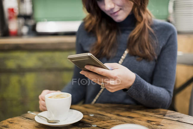Mujer revisando su smartphone en un café - foto de stock
