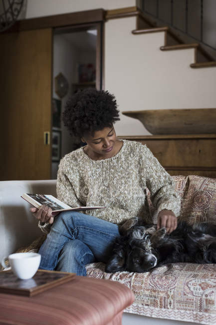 Молодая женщина сидит на диване и ласкает собаку. — стоковое фото