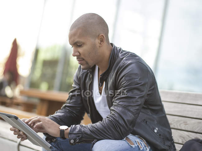 Junger Mann sitzt mit digitalem Tablet auf Bank — Stockfoto
