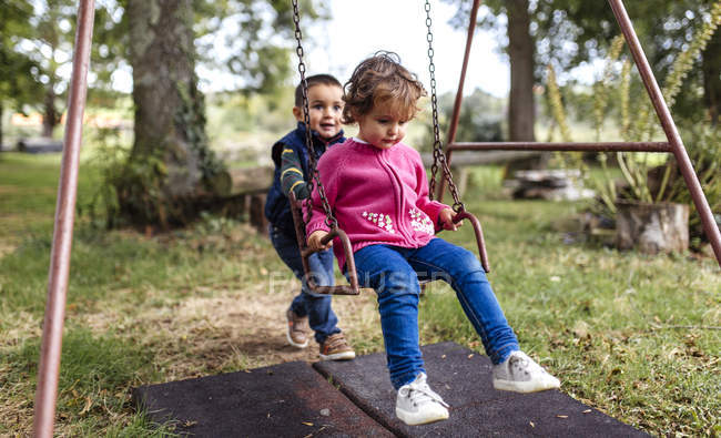 Toddler Boy Pushing Girl On Swing In Garden Two People