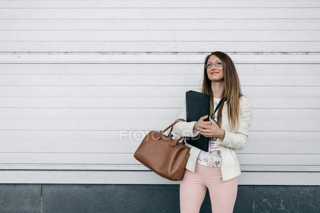 Femme d'affaires souriante tenant sac à main et dossier à l'extérieur — Photo de stock