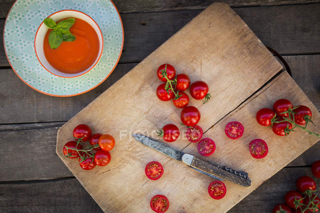 Bowl of tomato cream soup and chopping board with whole and sliced tomatoes — Stock Photo