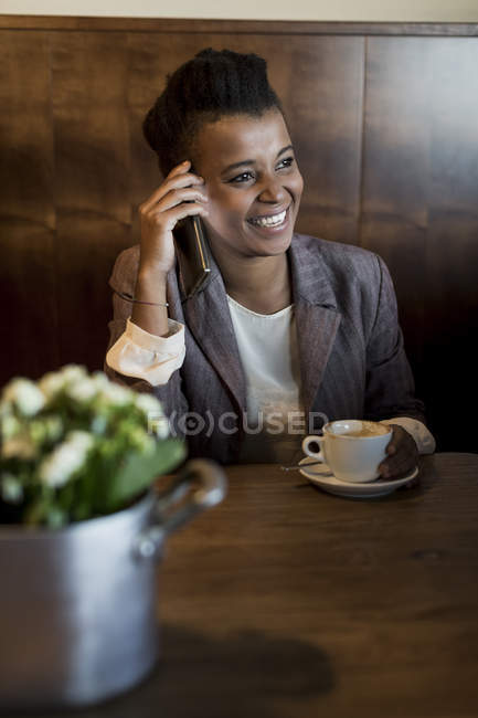 Портрет усміхненої молодої жінки, що сидить у кав'ярні, телефонуючи зі смартфоном — стокове фото