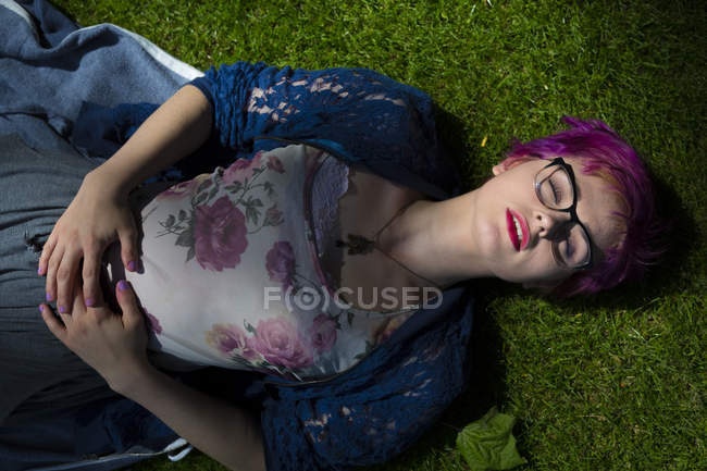 Retrato de mujer joven con el pelo teñido y los ojos cerrados acostado en un prado - foto de stock