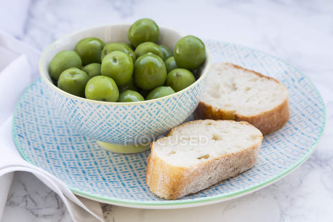Bowl of green olives and slices of bread on plate — Stock Photo