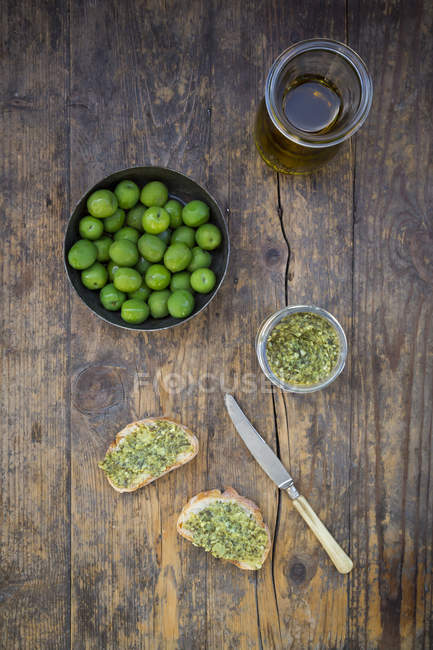 Bowls of green olives, carafe with olive oil, knife and slices of bread with spread — Stock Photo