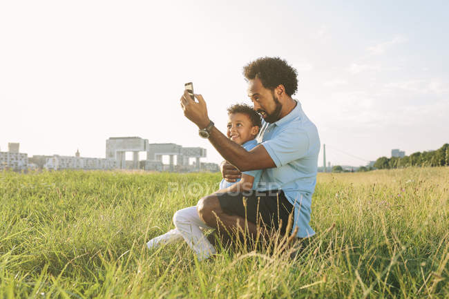 Feliz afroamericano padre e hijo en campo tomando selfie — exterior, chico  - Stock Photo | #178154076