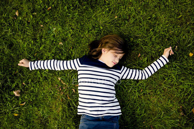 Девушка в полосатой толстовке лежит на лугу с закрытыми глазами — стоковое фото