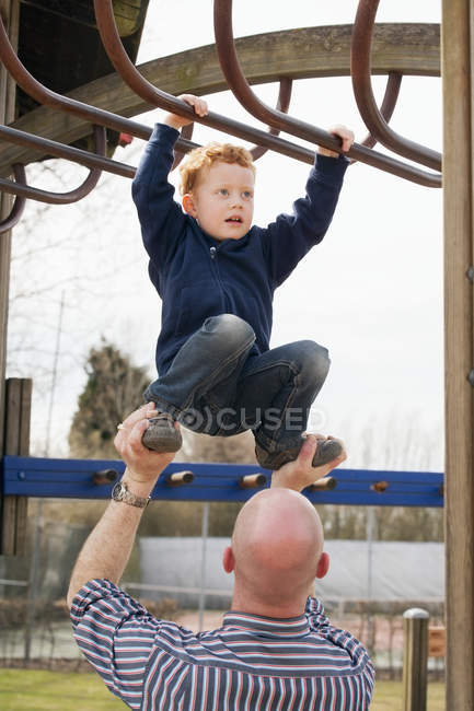 Padre ayudando a su hijo en el parque infantil escalada en el gimnasio selva - foto de stock