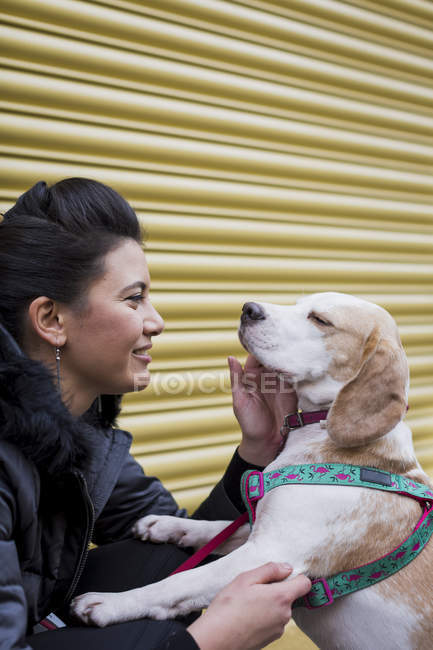 Woman stroking her dog in front of a roller shutter — Stock Photo