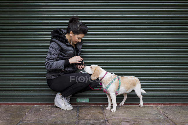 Woman and her dog on a sidewalk in front of a roller shutter — Stock Photo