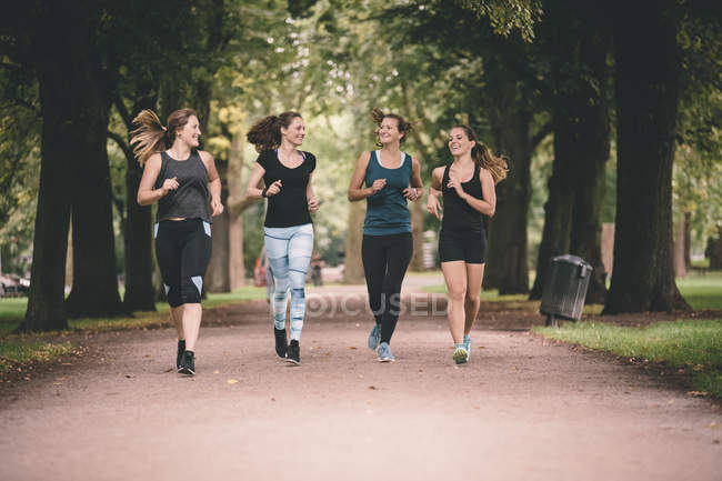 Quatro mulheres sorridentes correndo no parque — Fotografia de Stock