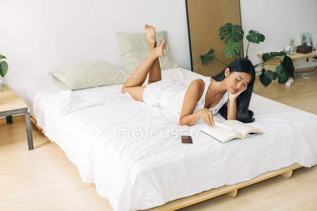Mujer joven acostada en la cama leyendo libro - foto de stock