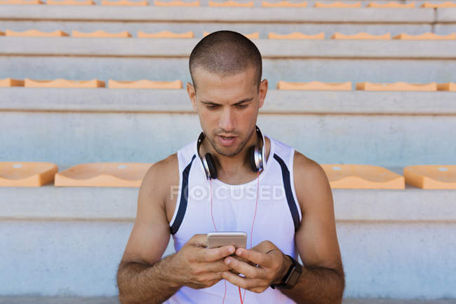 Young sportsman with headphones and smartphone — Stock Photo