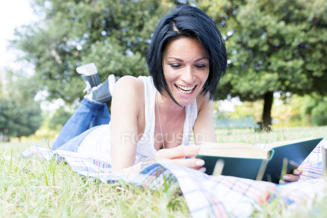 Laughing woman lying on a meadow reading a book — Stock Photo