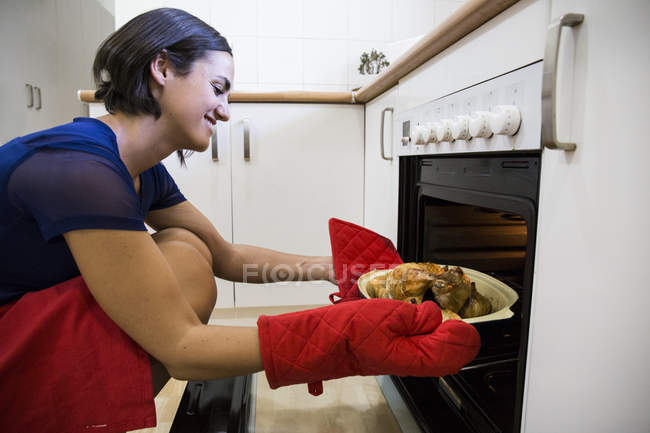 Vue latérale de la femme prenant du poulet rôti du four — Photo de stock