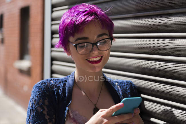 Retrato de una joven sonriente con el pelo teñido mirando su teléfono celular - foto de stock