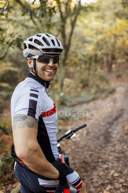 Portrait de vététiste souriant avec casque de vélo et lunettes de soleil dans la forêt — Photo de stock