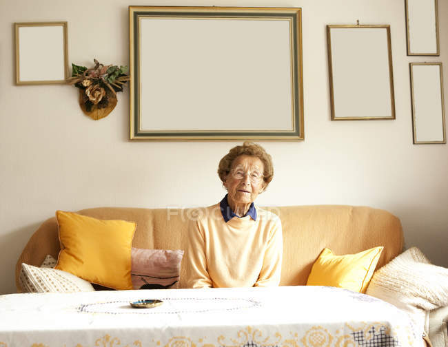Retrato de una mujer anciana sentada en un sofá en su sala de estar - foto de stock