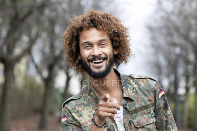 Portrait of smiling man with dyed ringlets wearing camouflage shirt pointing on viewer — beard, dyed hair - Stock Photo | #178182956 Portrait of smiling man with dyed ringlets wearing camouflage shirt pointing on viewer — beard, dyed hair - Stock Photo | #178182956