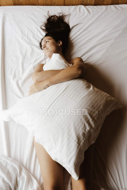 daydreaming woman lying on bed covering her body with a pillow