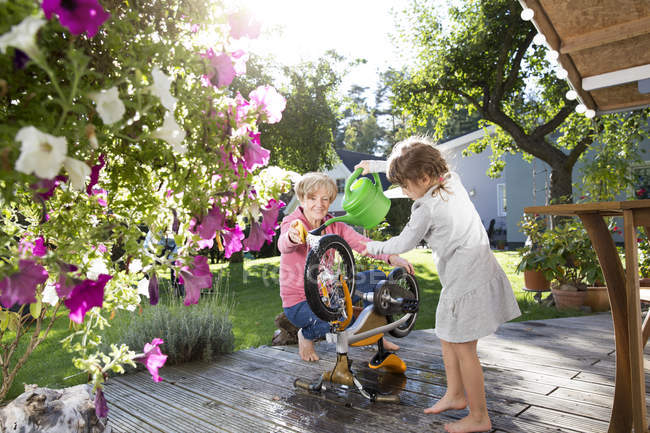 Бабушка и внучка стирают велосипед на террасе в саду — стоковое фото