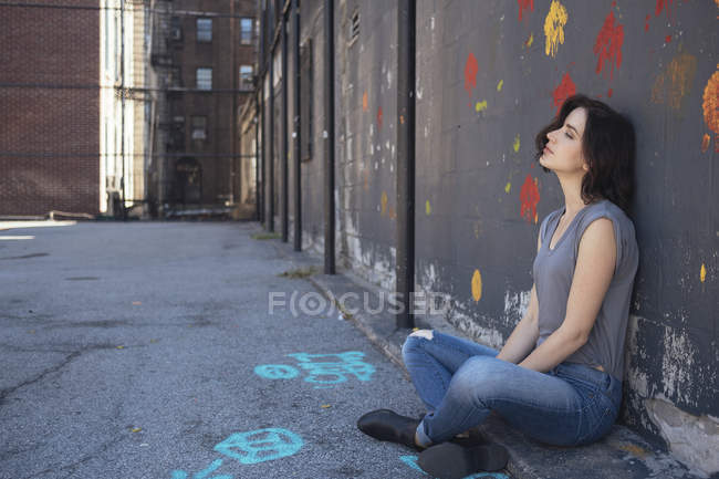 Jeune femme assise sur le sol appuyée contre un mur — Photo de stock