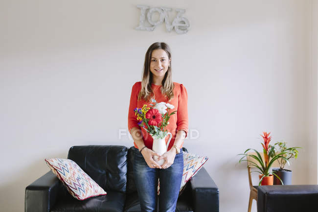Portrait of smiling young woman with bunch of flowers in her living room — Stock Photo