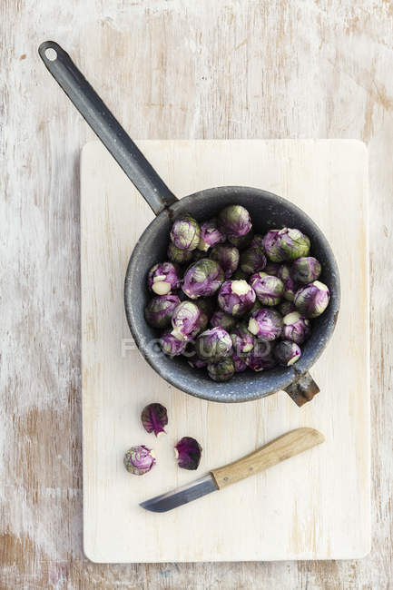 Red brussels sprouts in pot on chopping board and knife on shabby wooden surface — Stock Photo