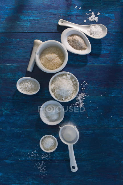 Bowls of different sorts of salt on blue wood — Stock Photo