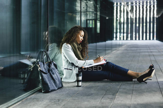 Junge Geschäftsfrau sitzt draußen und schreibt in Ordner — Stockfoto