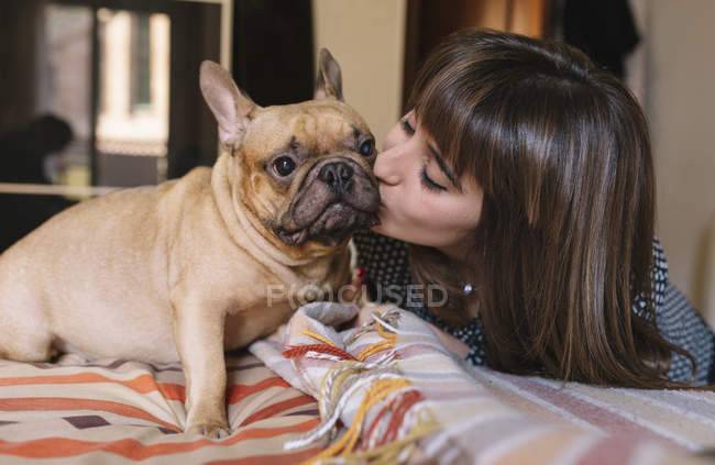 Giovane donna baciare il suo bulldog francese seduto sul letto — Foto stock