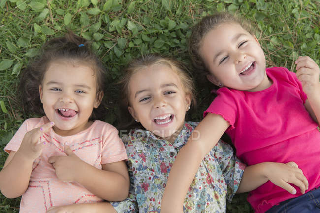 Ritratto di tre bambine che ridono accovacciate su un prato — Foto stock