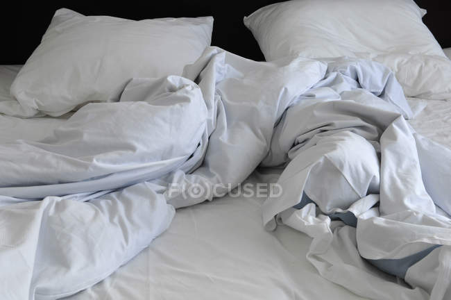 Vista diurna de la cama arrugada blanca con almohadas y manta - foto de stock