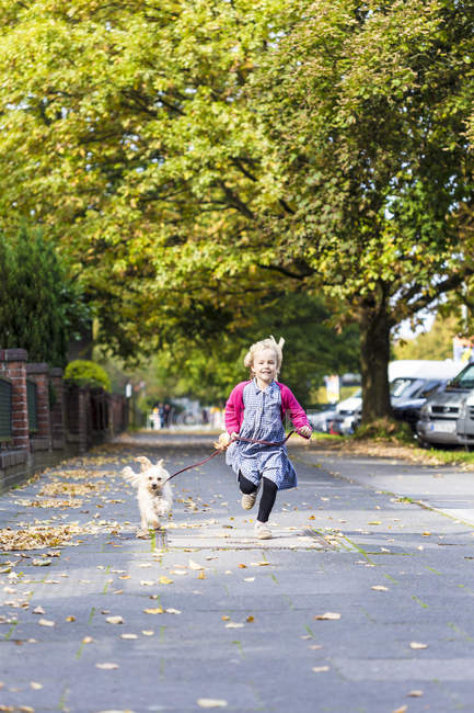 Girl running with mongrel on pavement — Stock Photo