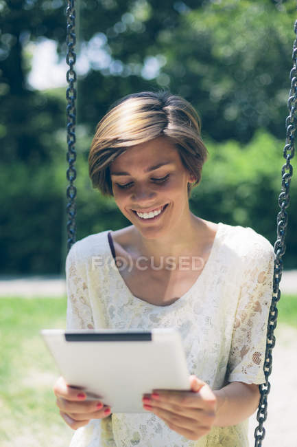 Happy teenage girl on a swing looking at digital tablet — Stock Photo
