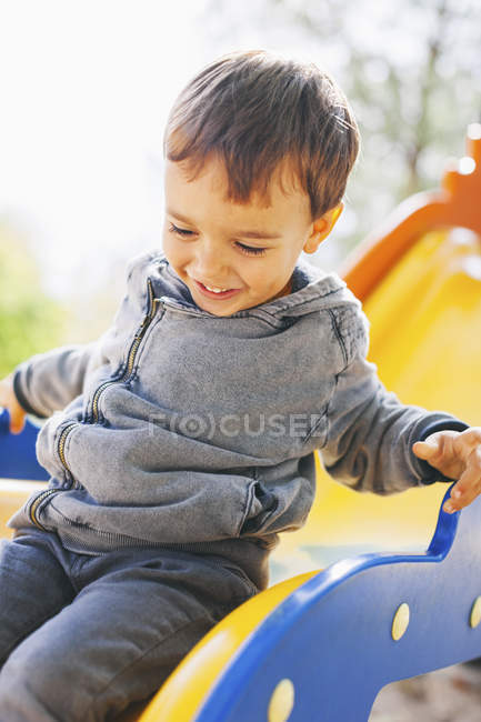 Niño feliz sentado en un tobogán en el patio de recreo — Stock Photo