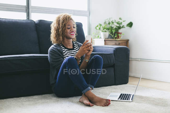 Mulher sentada no tapete e usando smartphone — Fotografia de Stock