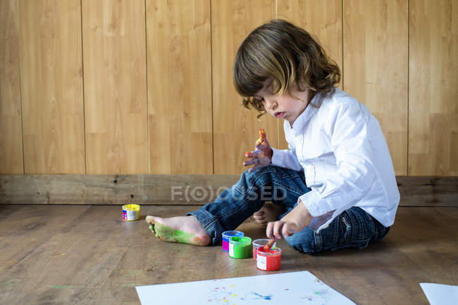 Little boy sitting on wooden floor using finger colours — Stock Photo