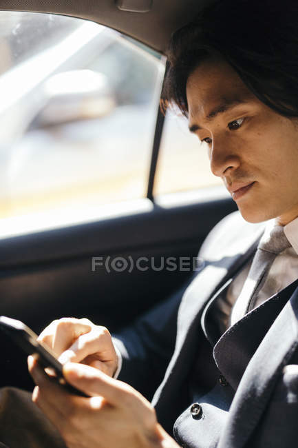 Uomo d'affari sul sedile posteriore della macchina utilizzando il telefono cellulare — Foto stock